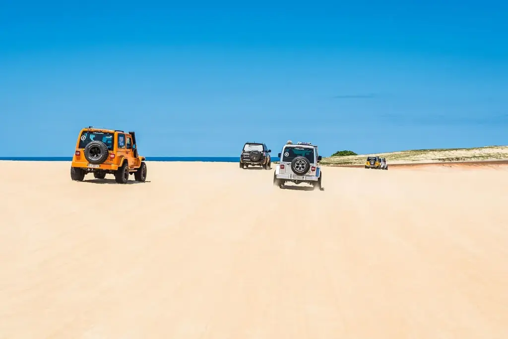 Buggy laranja e outros veículos atravessando as dunas de Genipabu