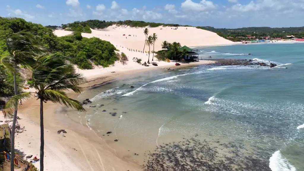 Vista da praia de Genipabu com dunas, coqueiros e mar.